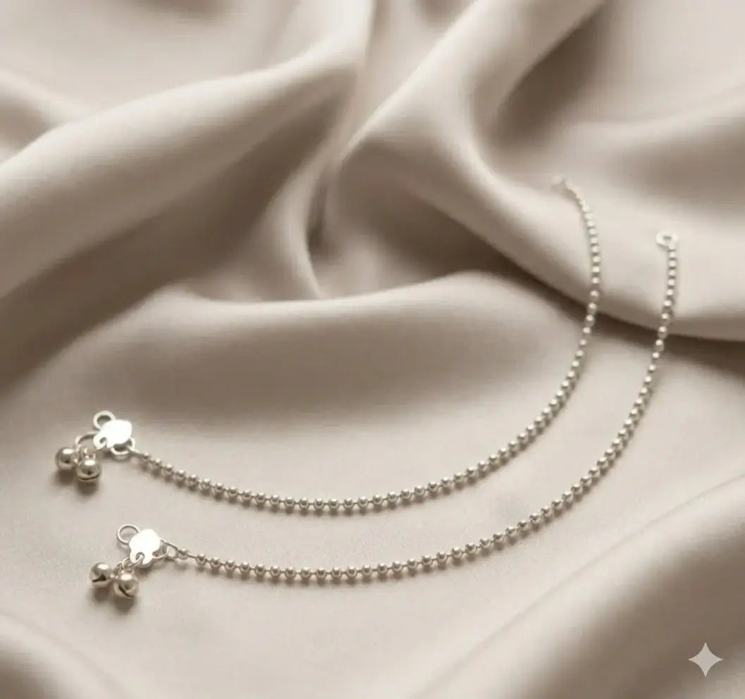 Indian payal silver and gold traditional anklet set featuring delicate bells on a soft fabric.